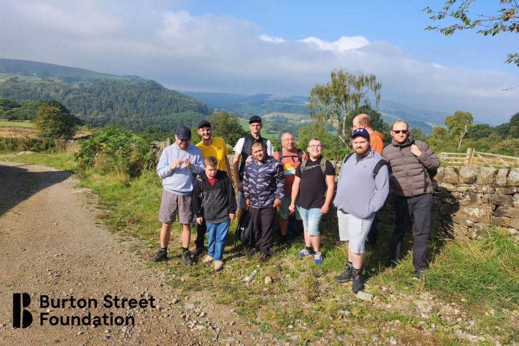 A diverse group of individuals gathered on a dirt road, engaged in conversation amidst a natural setting.