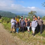 A diverse group of individuals gathered on a dirt road, engaged in conversation amidst a natural setting.