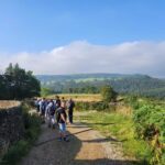 Several people strolling down a dusty road, enjoying a leisurely walk in a natural outdoor setting.