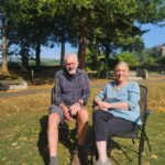 A man and woman sit together on chairs, enjoying a peaceful moment in a serene outdoor setting.