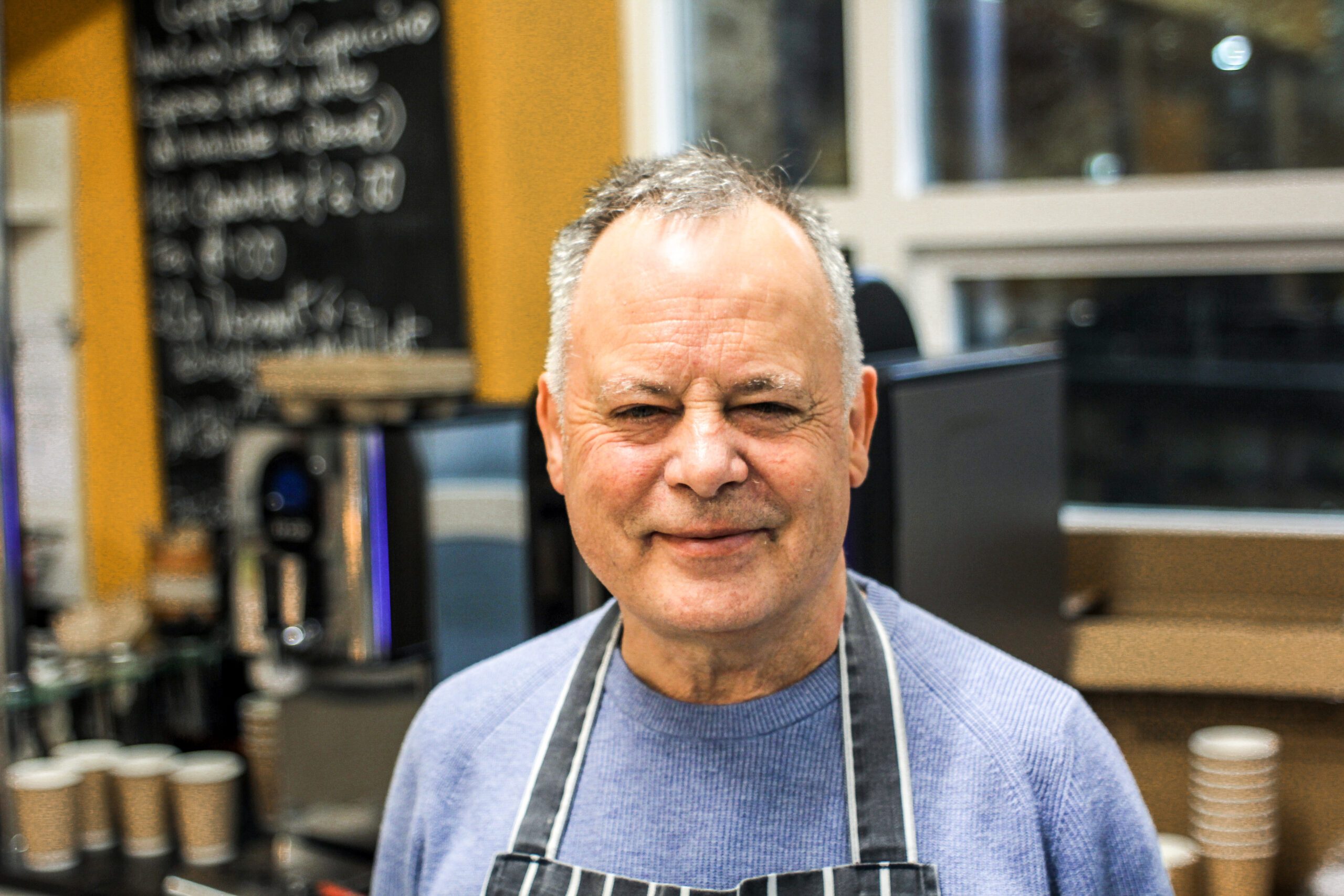 James smiling in a apron behind the cafe counter